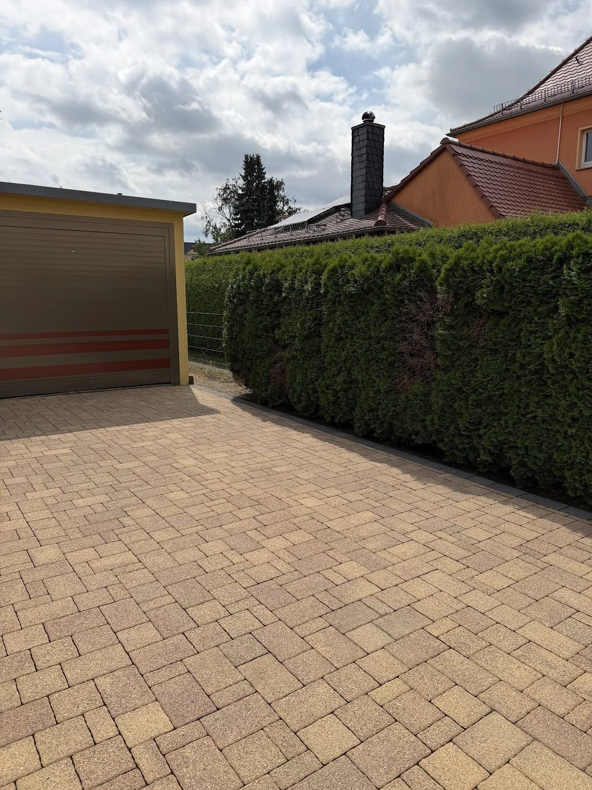 Frisch gereinigte, gepflasterte Einfahrt neben einer geschnittenen Hecke