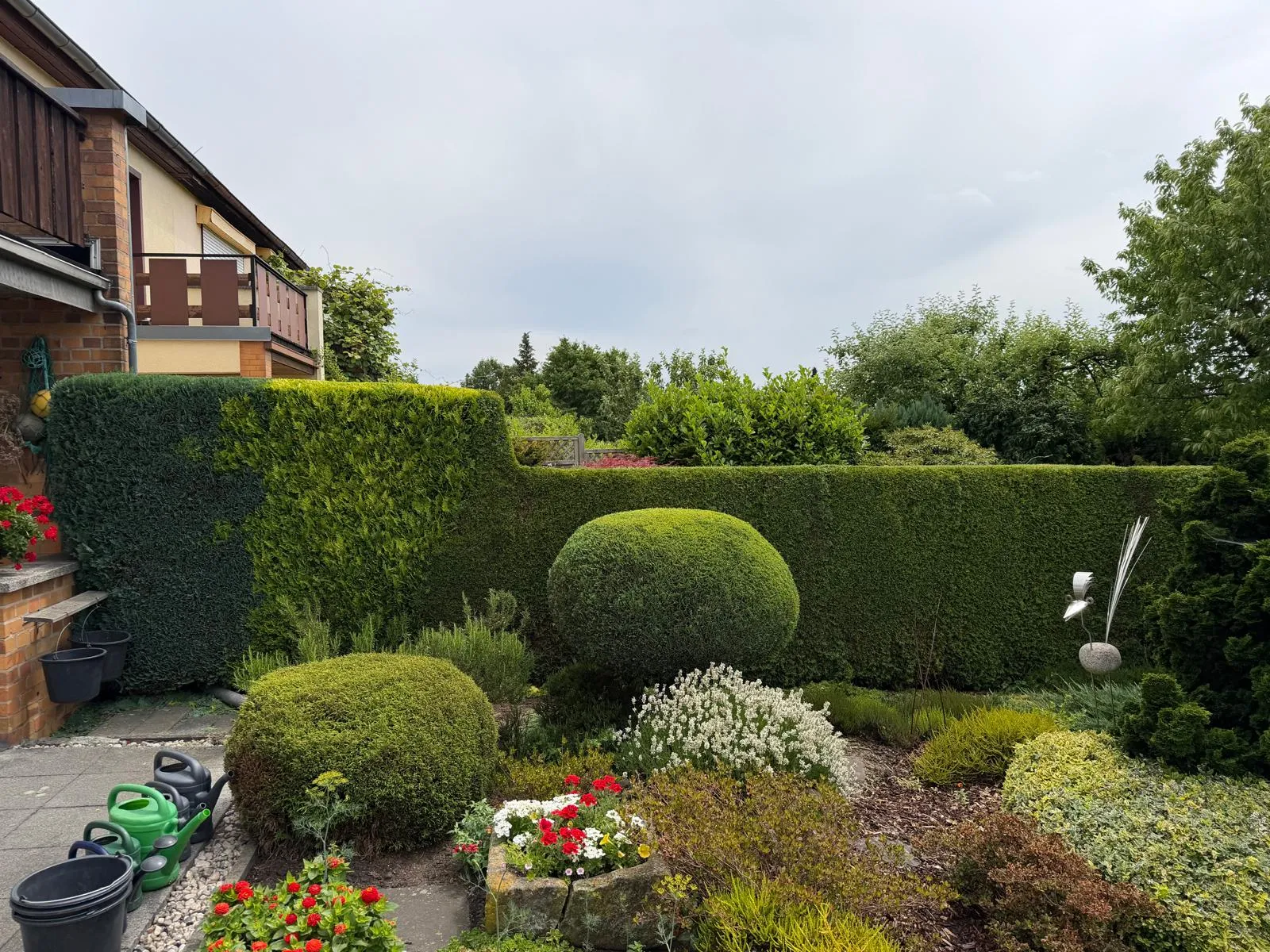 Gepflegter Garten mit blühenden Beeten, Formschnitt und Wohnhaus