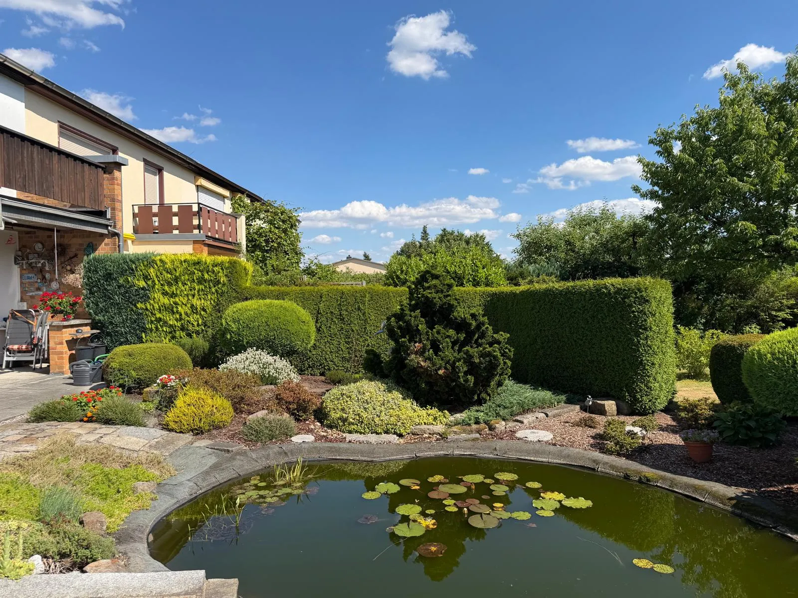 Gepflegter Garten mit Teich, Formschnitt-Hecken und blauem Himmel
